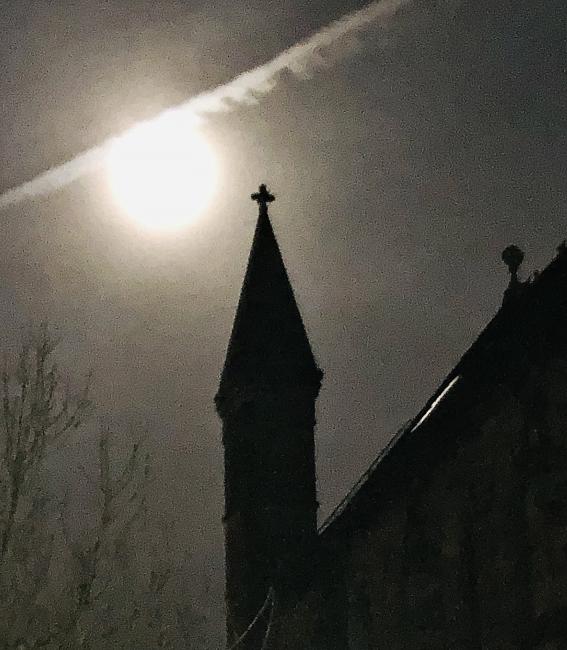 Vapour trail crossing moon above church