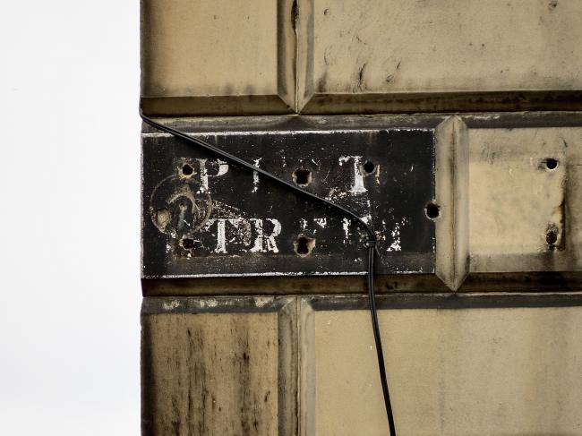 Faded street-name sign attached to masonry. White letters on black background reading PITT STREET.